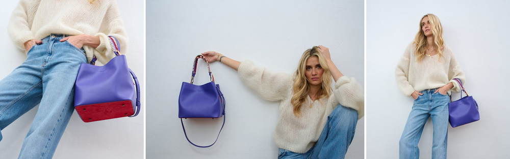 Woman holding a cobalt blue leather bag against a light wall.