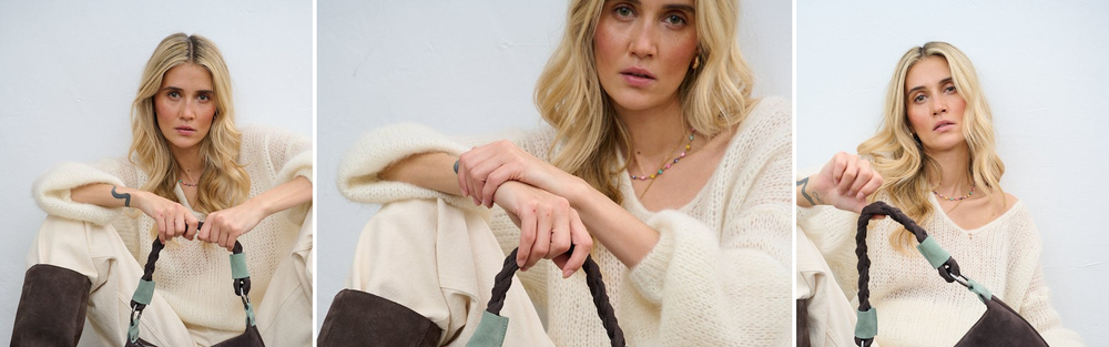 Woman in a cream knit holding a dark brown suede bag.