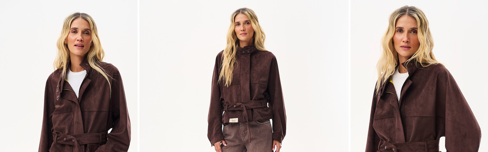 Woman in a short chocolate brown suede jacket belted at the waist, worn with a white top and brown jeans, studio photograph